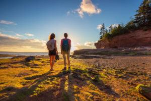 A young man and young woman hiking Burntcoat Head Park and enjoying a sunset view of the Atlantic Ocean tides flowing into the shores of the Bay of Fundy in Nova Scotia, Canada.